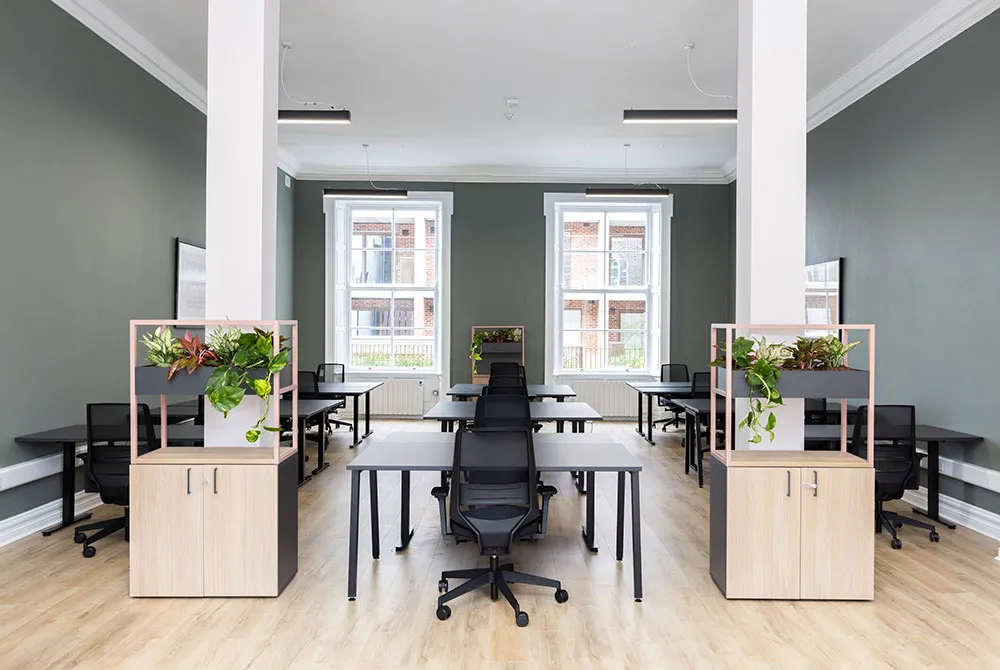 An open-plan office with desks, black task chairs and planters between white columns